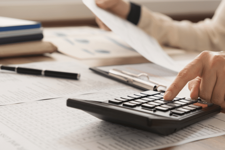 Hands using a calculator on a desk with documents and a clipboard nearby.