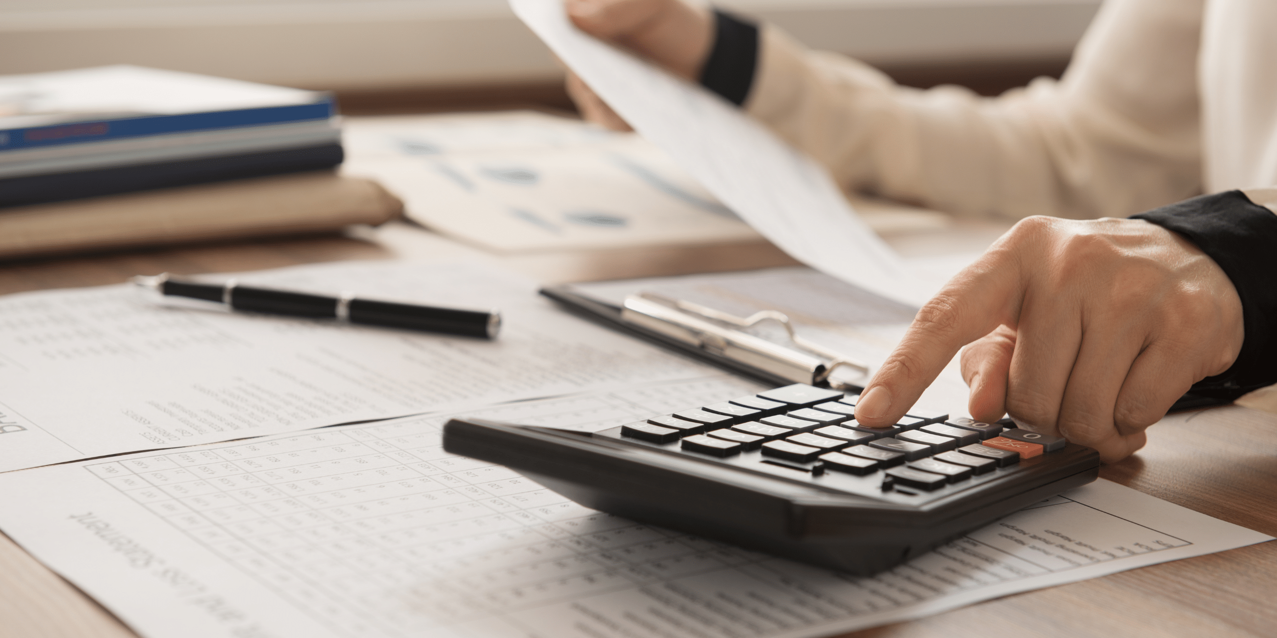 LJHHL_Blog_Buying_After_Seperation Hands using a calculator on a desk with documents and a clipboard nearby.