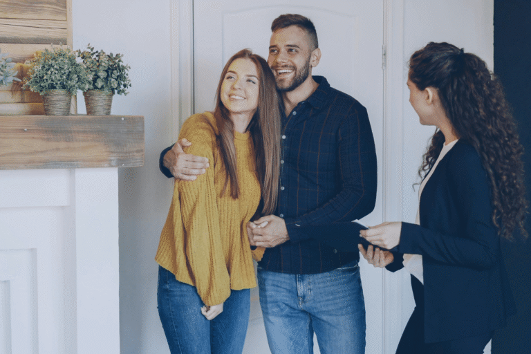 Couple smiles with a real estate agent indoors, likely a home tour or meeting to discuss a property.