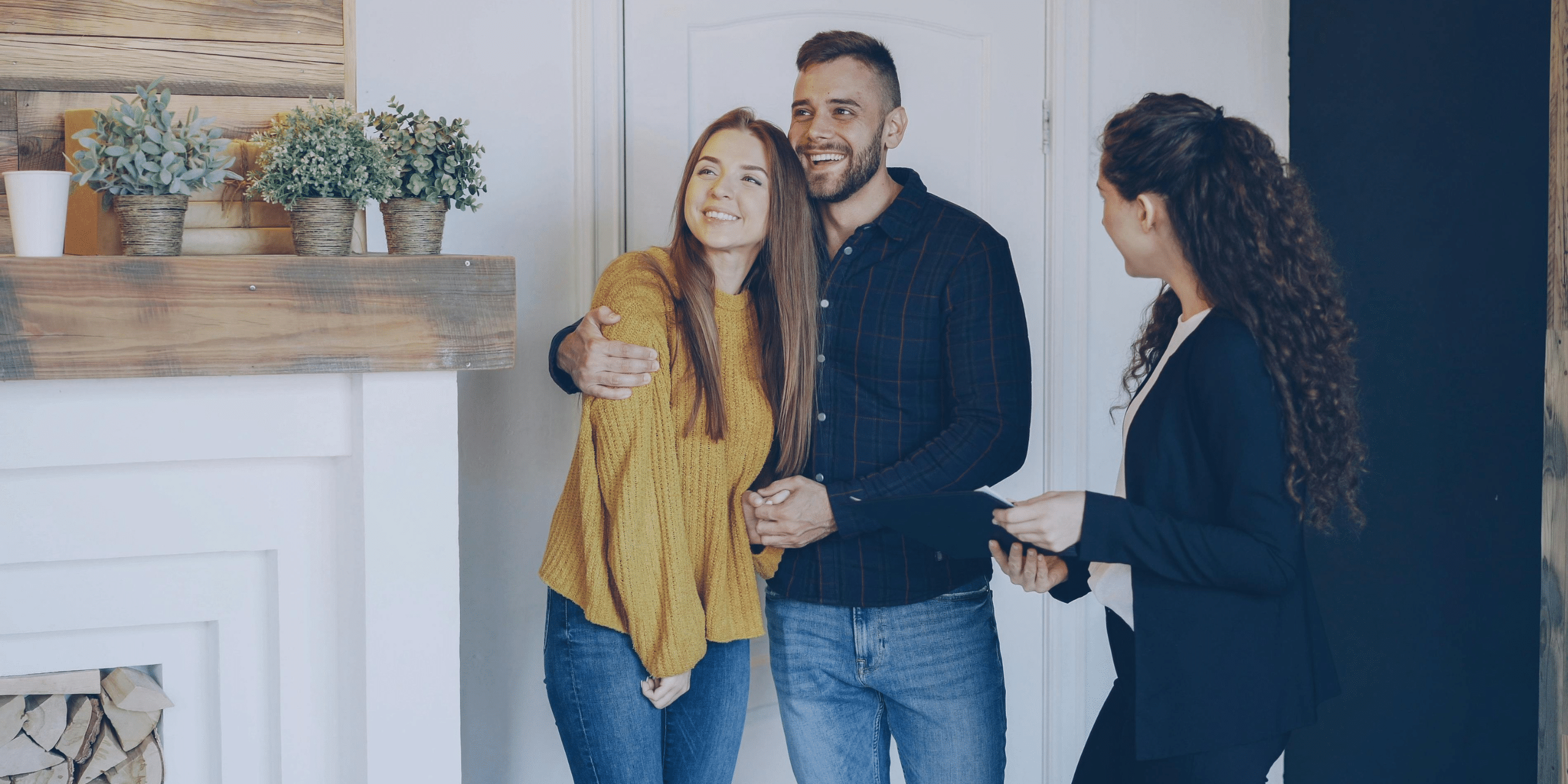 Couple smiles with a real estate agent indoors, likely a home tour or meeting to discuss a property.