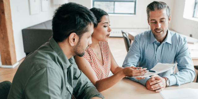 Three coworkers in a bright office review documents together at a round table, collaborating on a project.