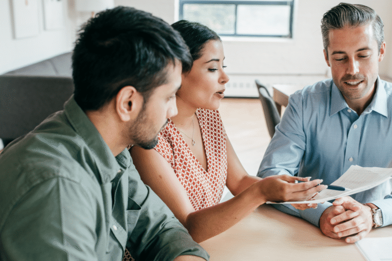 Three coworkers in a bright office review documents together at a round table, collaborating on a project.