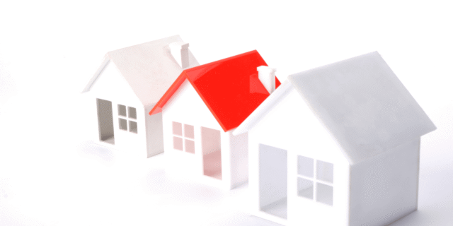 Paper houses model with a red-roofed house among white structures on a white background.