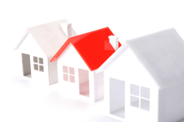 Paper houses model with a red-roofed house among white structures on a white background.