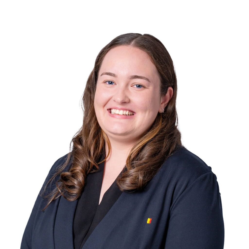 Smiling woman with long brown hair wearing a navy blazer against a white background.