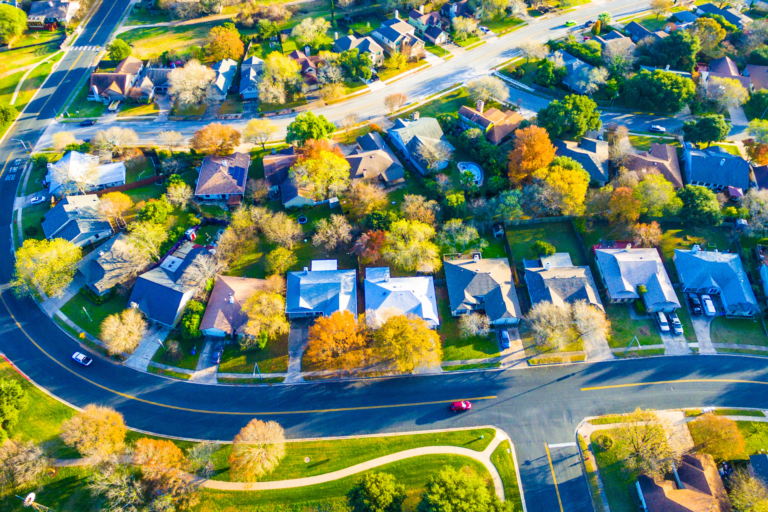 Aerial view of a suburban neighborhood with curved roads, green lawns, and tree-lined houses from above.